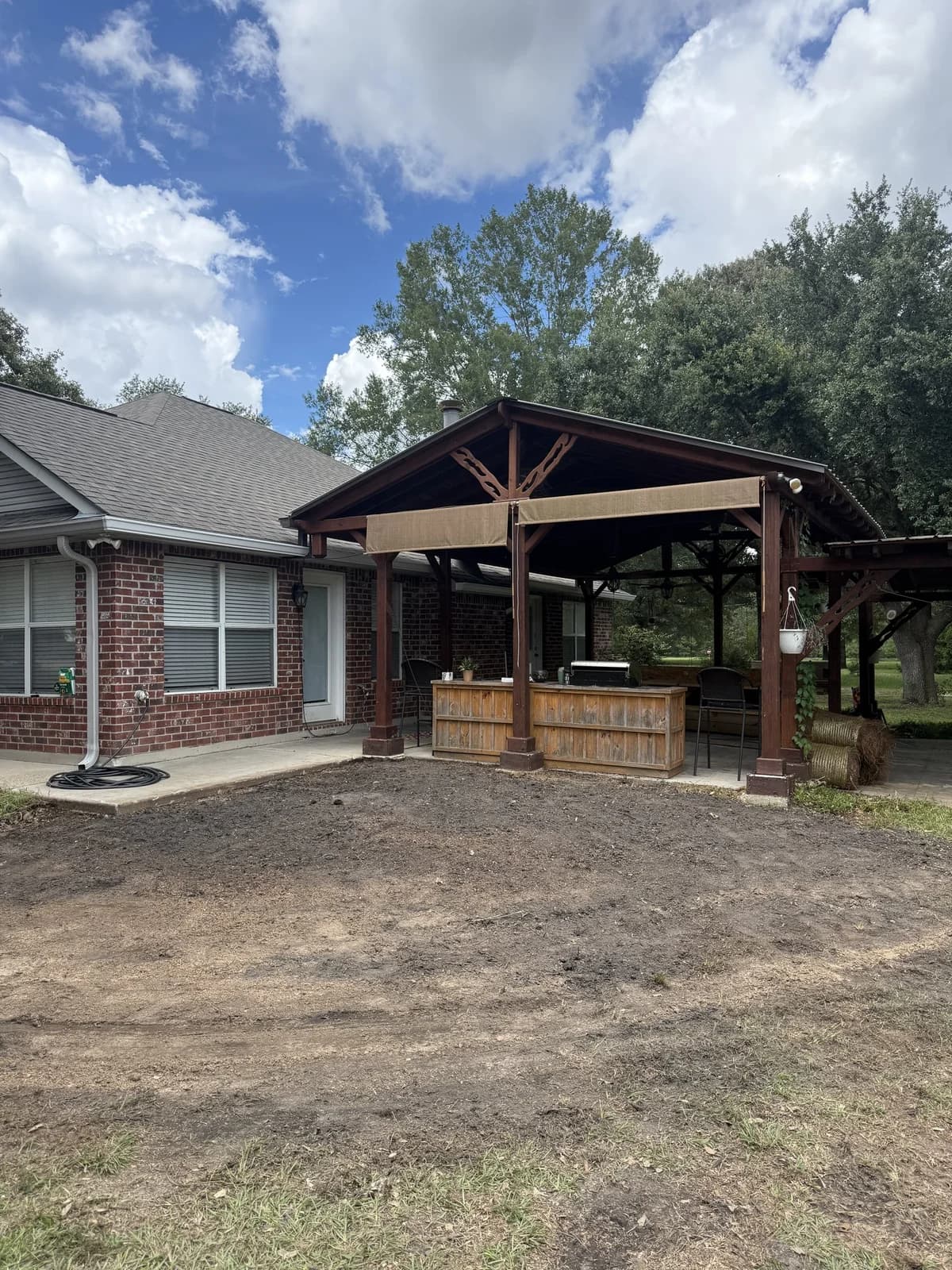 Same corner cleared to bare dirt, stump gone, patio and outdoor kitchen fully visible